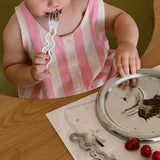 Child in a pink and white striped dress holding a fork, with a plate and raspberries on a table.